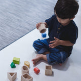 A child sitting on a floor playing with the PlanToys Geo Matching Blocks. 
