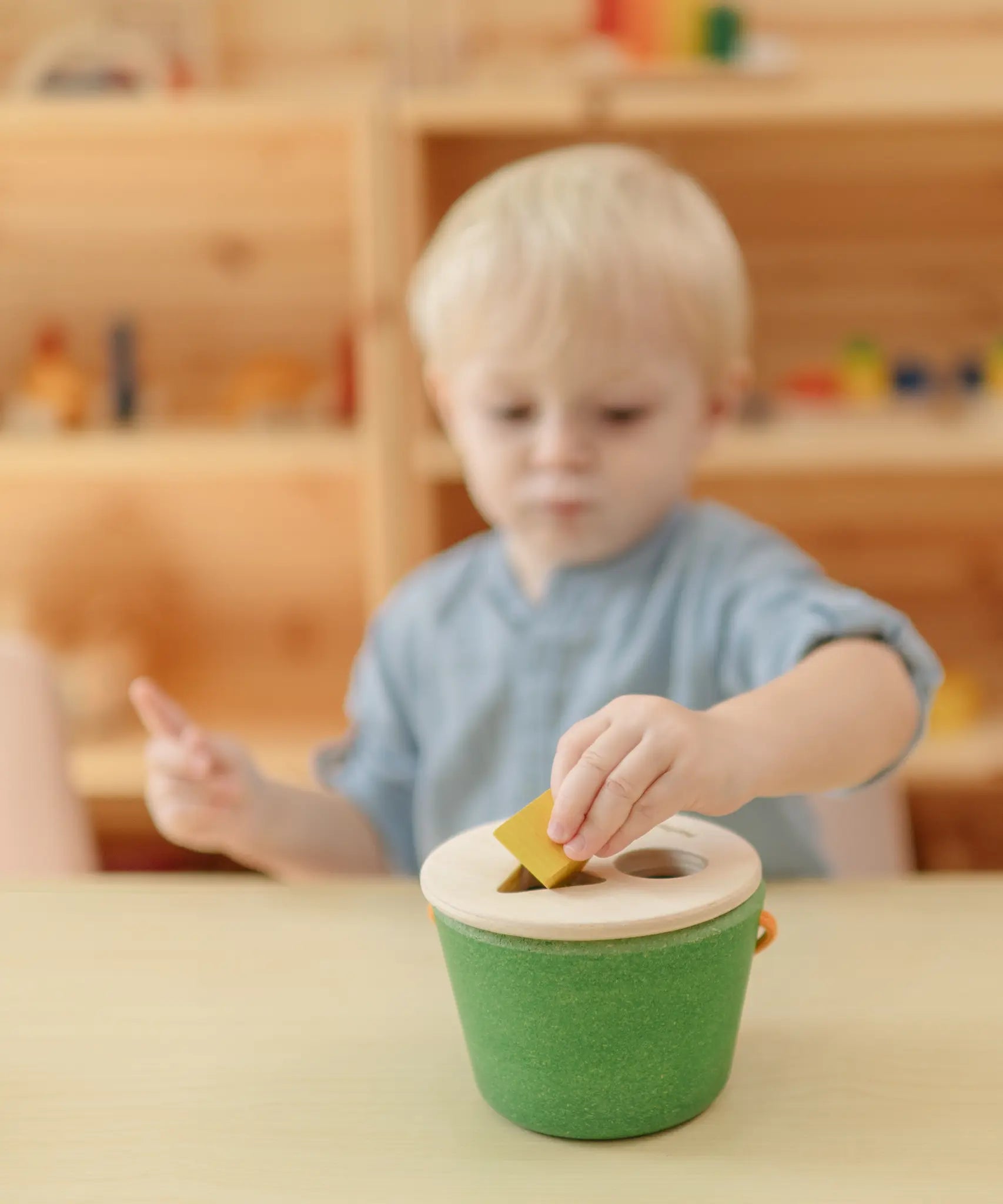 Child placing the yellow cube into the PlanToys geo sorting bucket wooden shape sorting toy. 