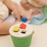 Child placing block into the slots on the PlanToys geo sorting bucket wooden shape sorting toy. 