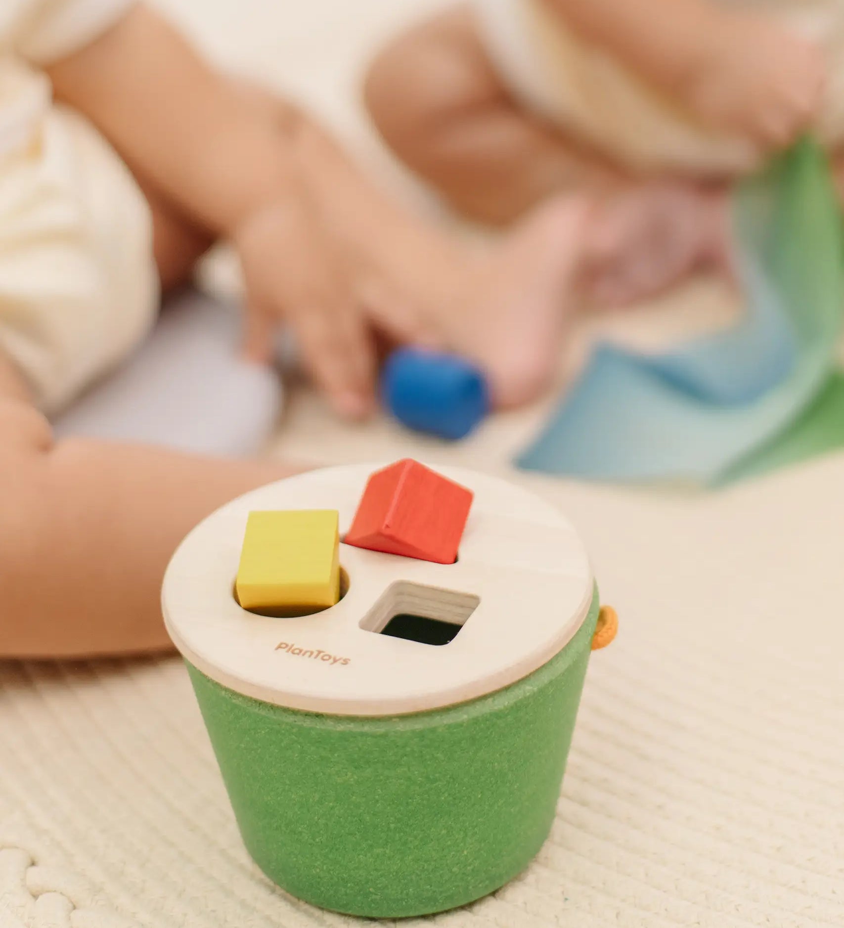 Child placing block into the slots on the PlanToys geo sorting bucket wooden shape sorting toy. 