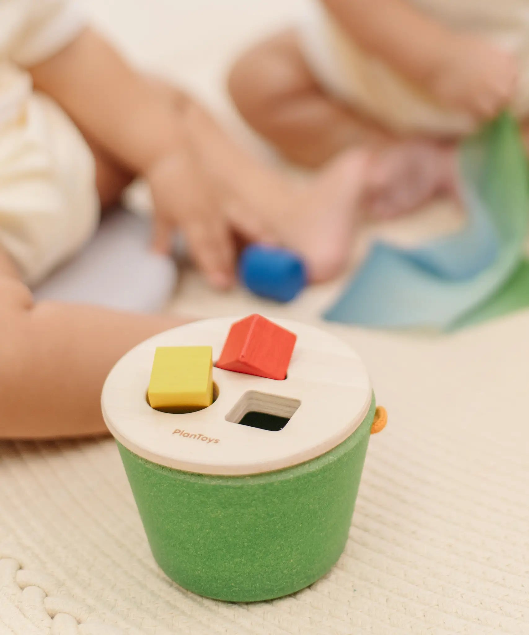 Child placing block into the slots on the PlanToys geo sorting bucket wooden shape sorting toy. 