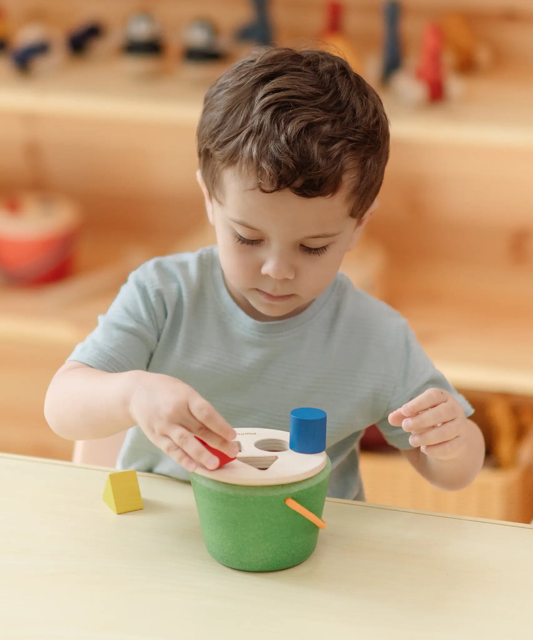 Child playing with the PlanToys geo sorting bucket wooden shape sorting toy. 