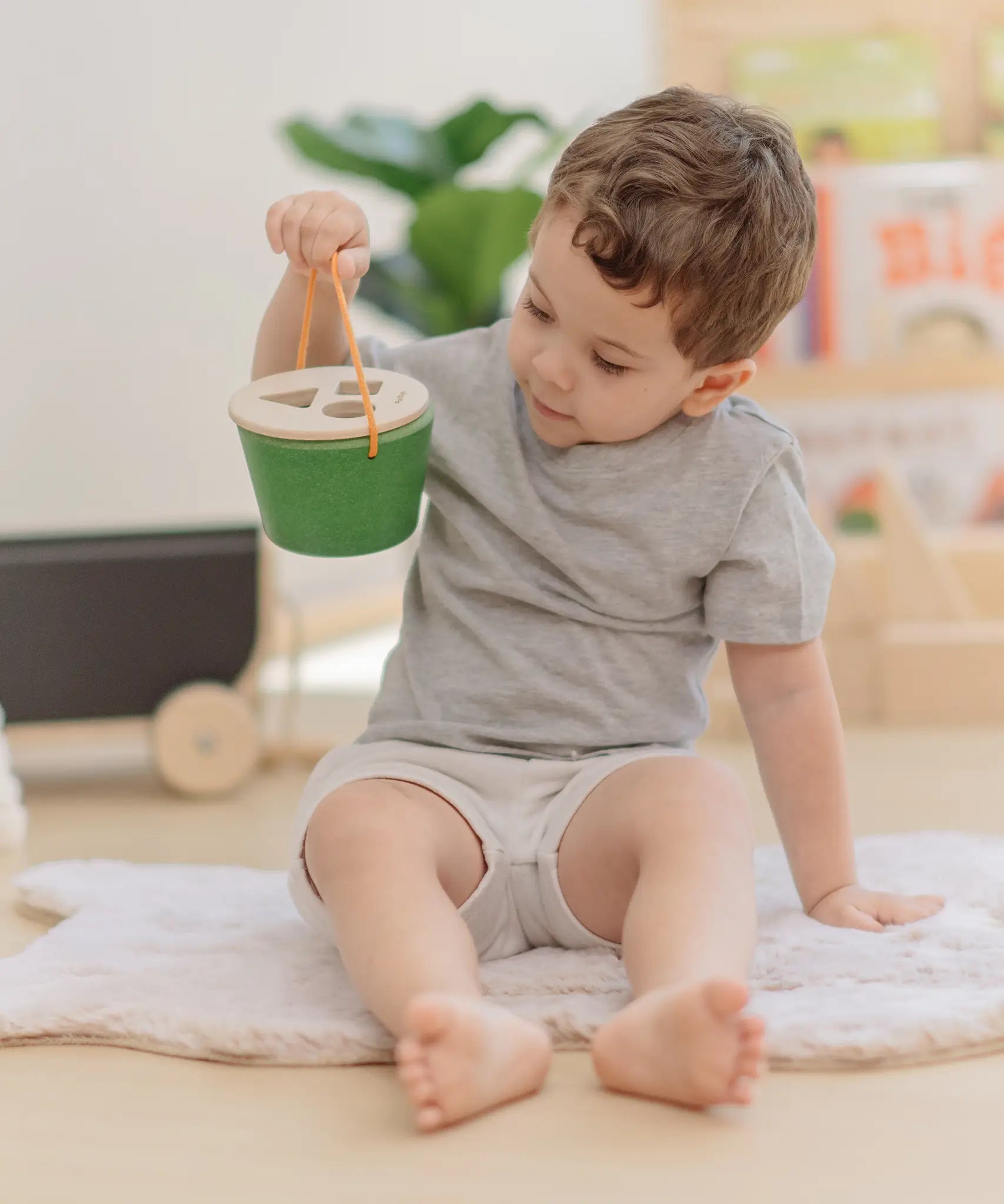 Child holding the PlanToys geo sorting bucket wooden shape sorting toy in their hand. 