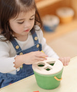 Child placing the yellow block into the green PlanToys geo sorting bucket wooden shape sorting toy. 