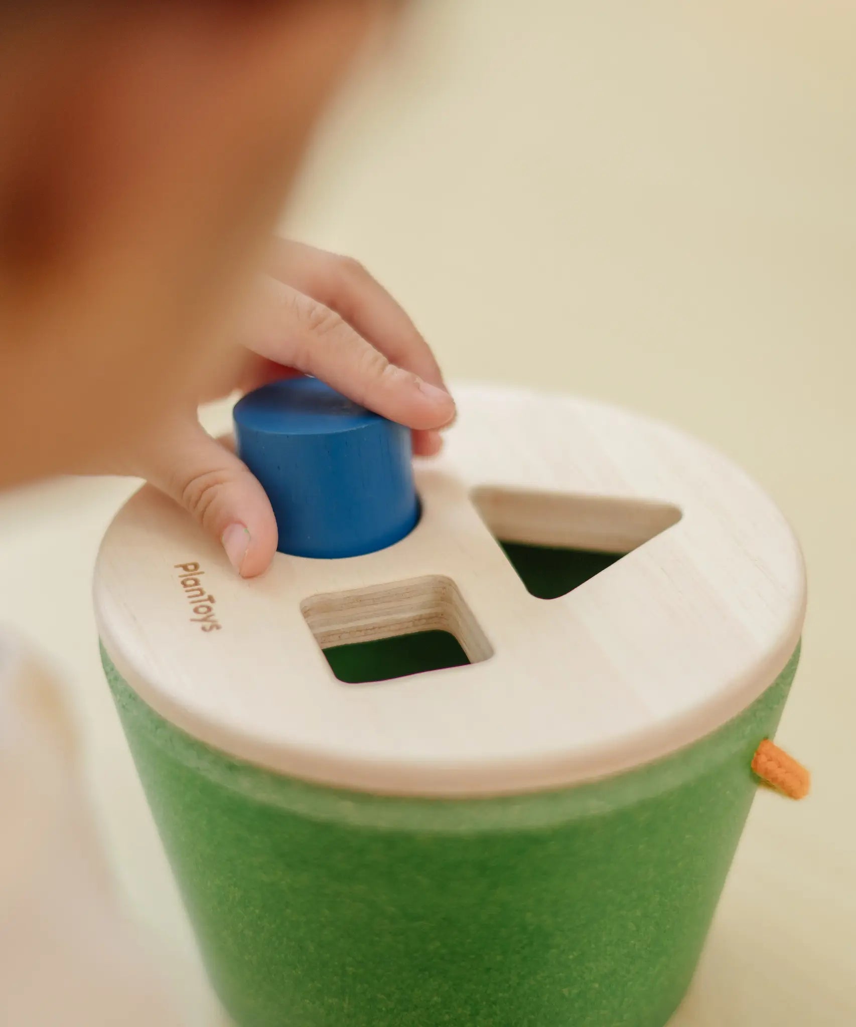 Close up of child placing the blue cylinder into the PlanToys geo sorting bucket wooden shape sorting toy. 