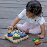 A child sitting on wooden decking playing with the PlanToys Geometric Sorting Board. They are placing the yellow coloured circle piece on top of the other circles. 