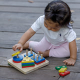 A child sitting on wooden decking playing with the PlanToys Geometric Sorting Board. They are placing the yellow coloured circle piece on top of the other circles. 