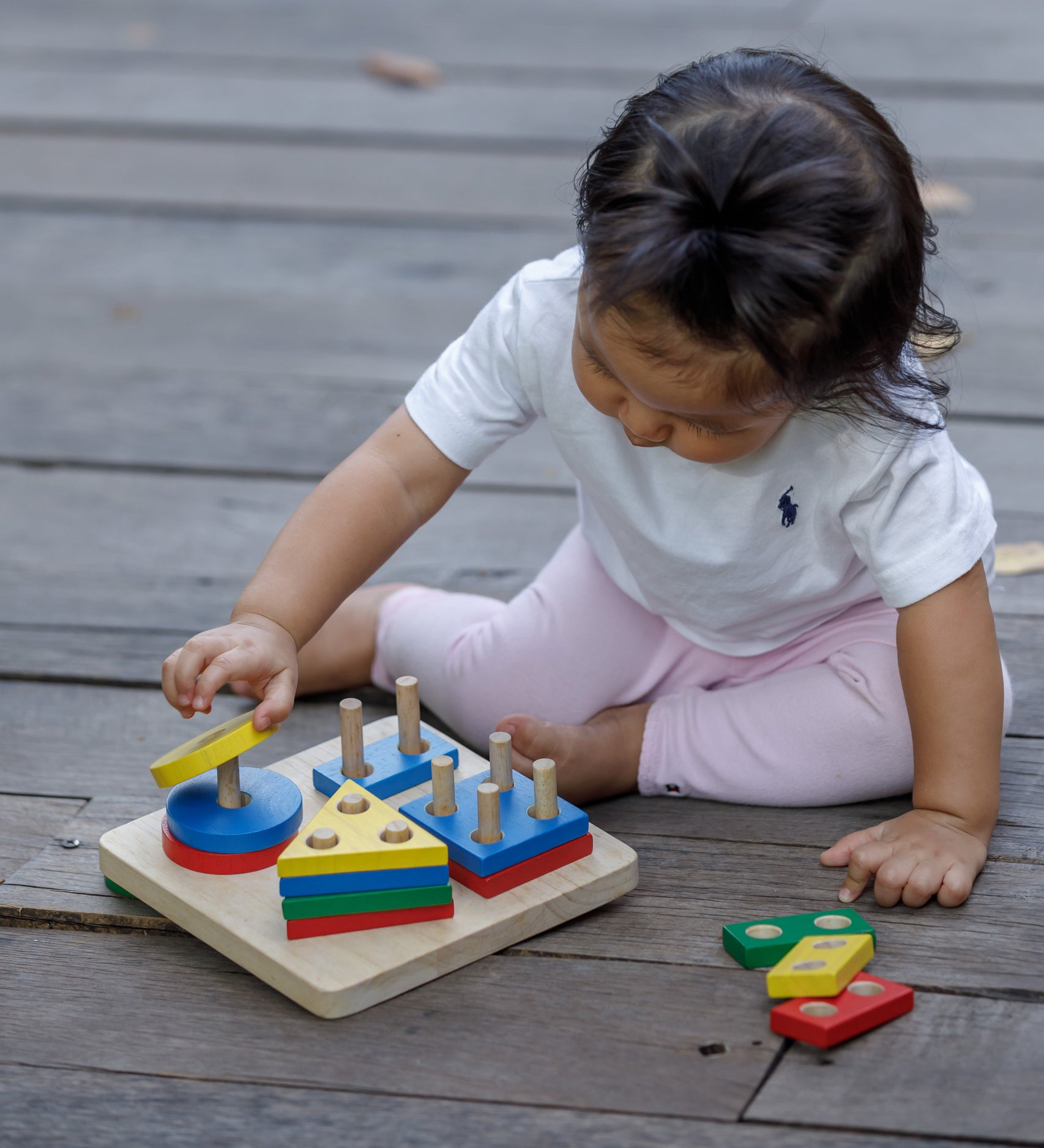 A child sitting on wooden decking playing with the PlanToys Geometric Sorting Board. They are placing the yellow coloured circle piece on top of the other circles. 