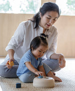 A toddler playing with the PlanToys Geometric Sorting toy, an adult is sitting behind them. 