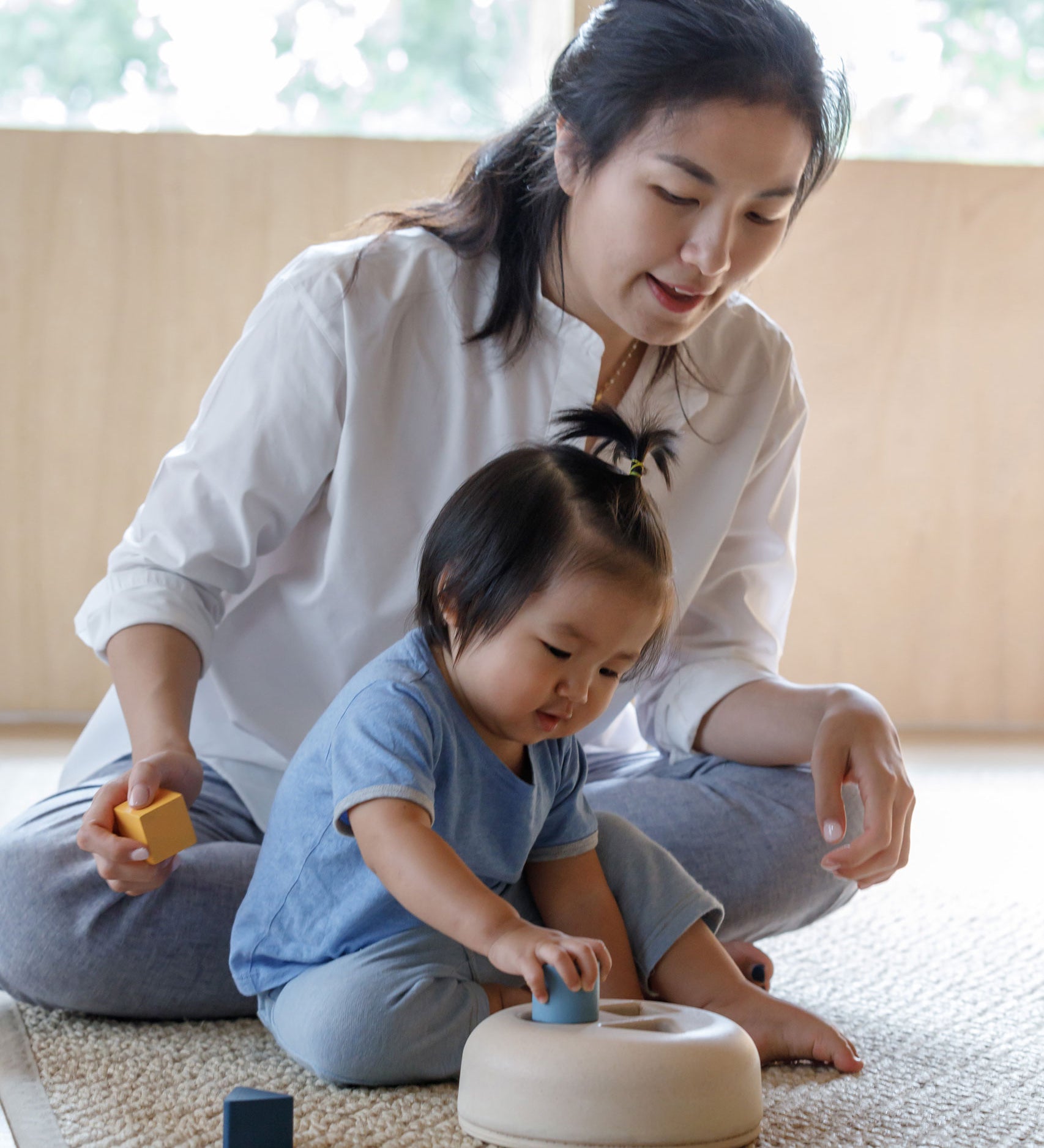 A toddler playing with the PlanToys Geometric Sorting toy, an adult is sitting behind them. 