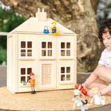 Chil playing with the PlanToys wooden Georgian dollhouse children's toy. Wooden dolls have been placed on the roof and outside the house.