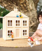 Chil playing with the PlanToys wooden Georgian dollhouse children's toy. Wooden dolls have been placed on the roof and outside the house.