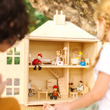 Close up of children playing with the PlanToys wooden Georgian dollhouse children's toy. The house has been filled with dolls house furniture.