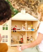 Close up of children playing with the PlanToys wooden Georgian dollhouse children's toy. The house has been filled with dolls house furniture.