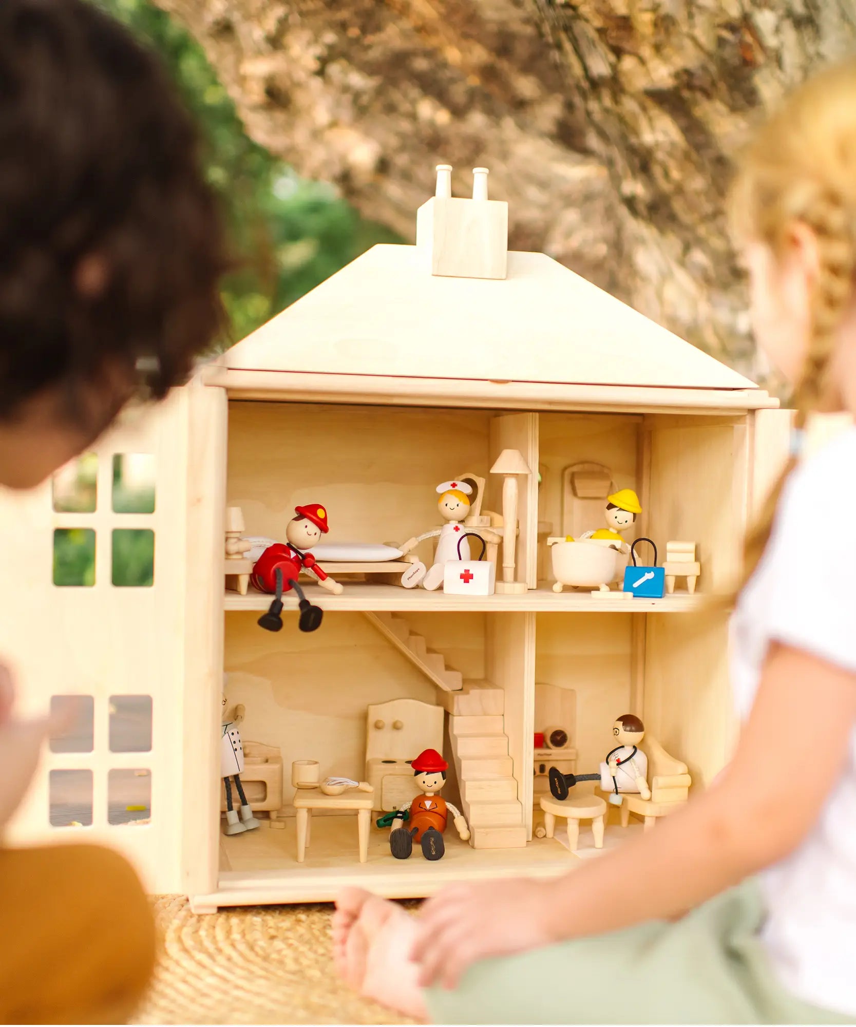 Close up of children playing with the PlanToys wooden Georgian dollhouse children's toy. The house has been filled with dolls house furniture.