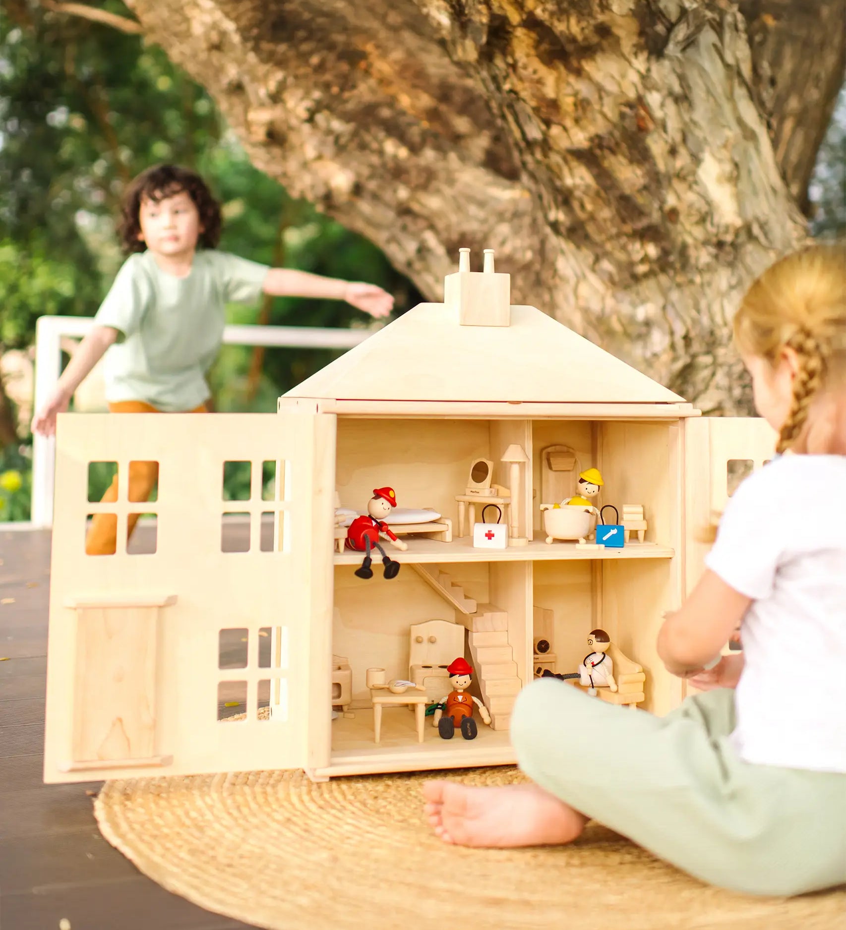 Children playing with the PlanToys wooden Georgian dollhouse children's toy. The house has been filled with dolls house furniture.