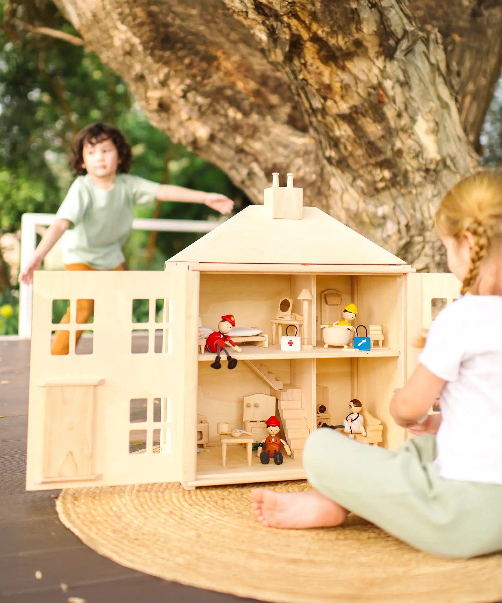Children playing with the PlanToys wooden Georgian dollhouse children's toy. The house has been filled with dolls house furniture.