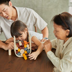 A family sitting around a table playing with the PlanToys Giant Beaver Tumble game. 