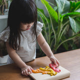 A child stood by the side of a wooden table playing with the PlanToys Giraffe Puzzle. 
