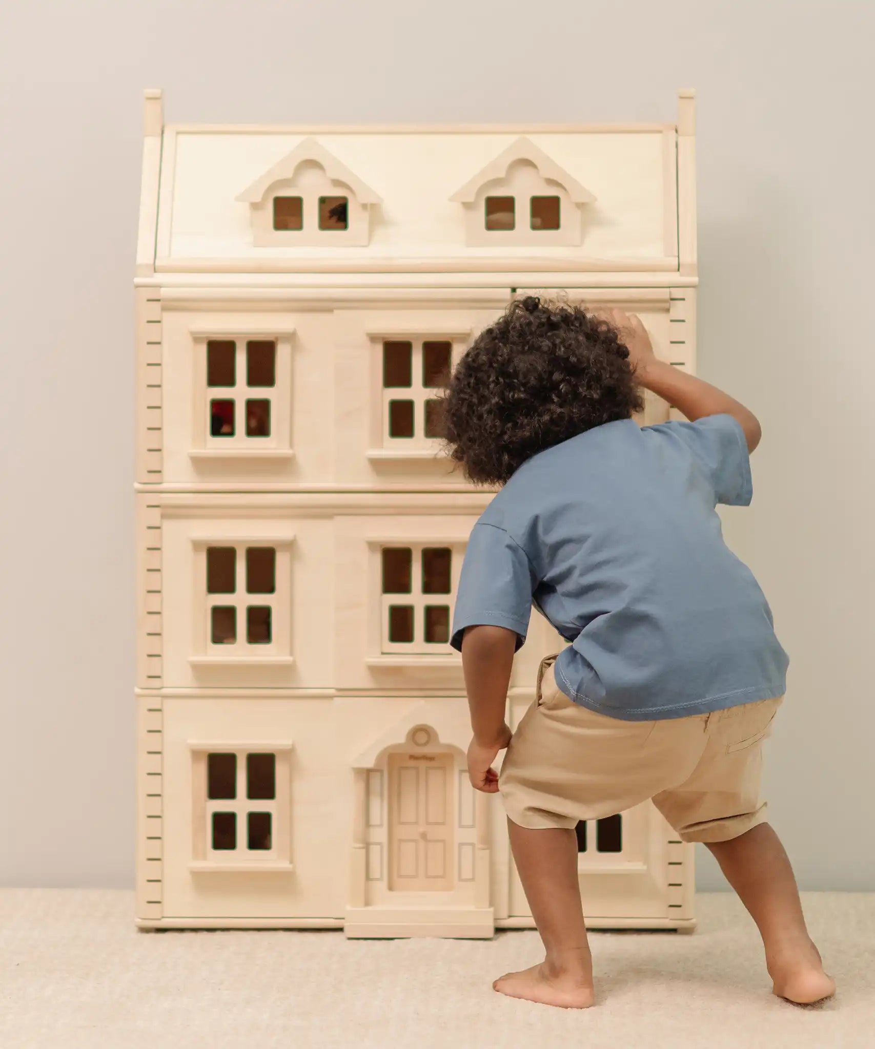 Child looking through the window of the PlanToys Grand Victorian Dollhouse. 