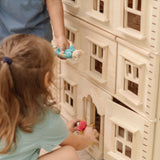 Close up of children playing with the PlanToys Grand Victorian Dollhouse. They are placing doll in the house through the front door. 