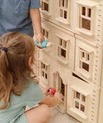 Close up of children playing with the PlanToys Grand Victorian Dollhouse. They are placing doll in the house through the front door. 
