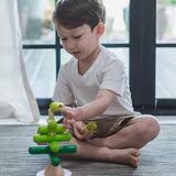 A child playing with the PlanToys Stacking Tree Wooden Toy. The child is placing the green pieces onto the base piece. 