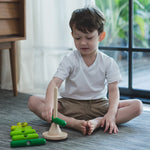 A child playing with the PlanToys Stacking Tree Wooden Toy. The child has placed the longest dark green base on the base. 