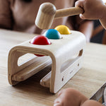 A close up of a child's hands playing with the PlanToys Hammer Balls, they are holding onto the hammer aiming at the red ball.