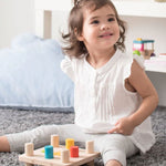 A young child sitting on a grey coloured rug playing with the PlanToys Hammer Peg wooden toy. 