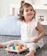 A young child sitting on a grey coloured rug playing with the PlanToys Hammer Peg wooden toy. 
