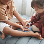 Close up of children playing with the PlanToys wooden touch and guess sensory game on a grey sofa.