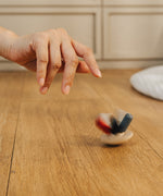 A hand shown spinning the PlanToys Flexi Jellyfish wooden high contrast baby toy. A wooden top with high contrast, white, greys, black and red flexible wooden pieces for the jellyfish legs. PlanToys range of toys are made from sustainably sourced rubberwood, we're proud stockists of PlanToys here at Babipur. 