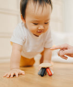 A baby crawling towards the PlanToys Flexi Jellyfish wooden high contrast baby toy. A wooden top with high contrast, white, greys, black and red flexible wooden pieces for the jellyfish legs. PlanToys range of toys are made from sustainably sourced rubberwood, we're proud stockists of PlanToys here at Babipur. 