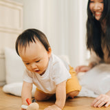 A baby crawling towards the PlanToys Flexi Jellyfish wooden high contrast baby toy. A wooden top with high contrast, white, greys, black and red flexible wooden pieces for the jellyfish legs. PlanToys range of toys are made from sustainably sourced rubberwood, we're proud stockists of PlanToys here at Babipur. 