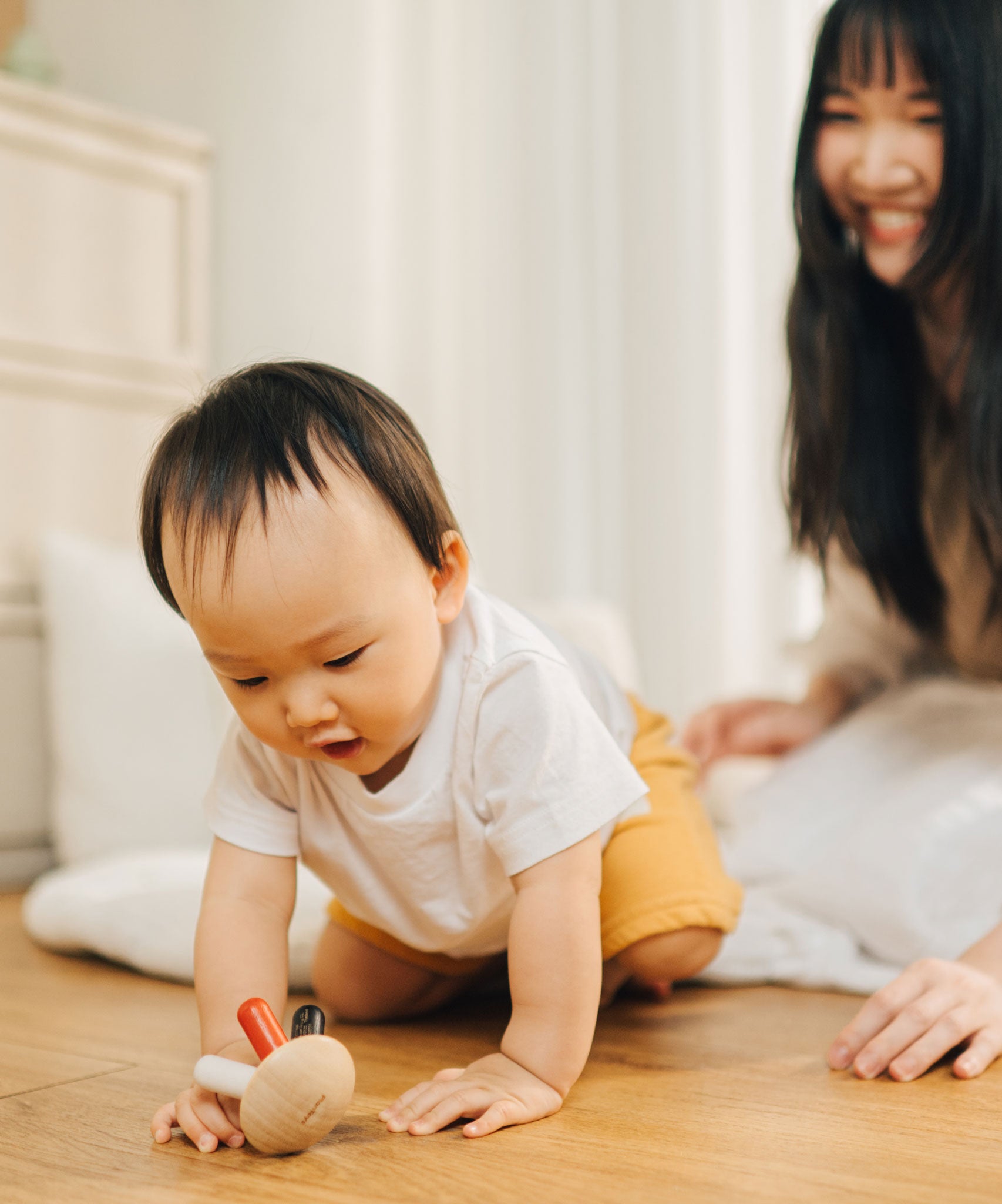 A baby crawling towards the PlanToys Flexi Jellyfish wooden high contrast baby toy. A wooden top with high contrast, white, greys, black and red flexible wooden pieces for the jellyfish legs. PlanToys range of toys are made from sustainably sourced rubberwood, we're proud stockists of PlanToys here at Babipur. 