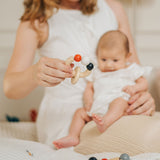 An adult holding a baby on their lap with a PlanToys Beads Rattle in a High Contrast colourway in their other hand. PlanToys range of toys are made from sustainably sourced rubberwood, we're proud stockists of PlanToys here at Babipur. 