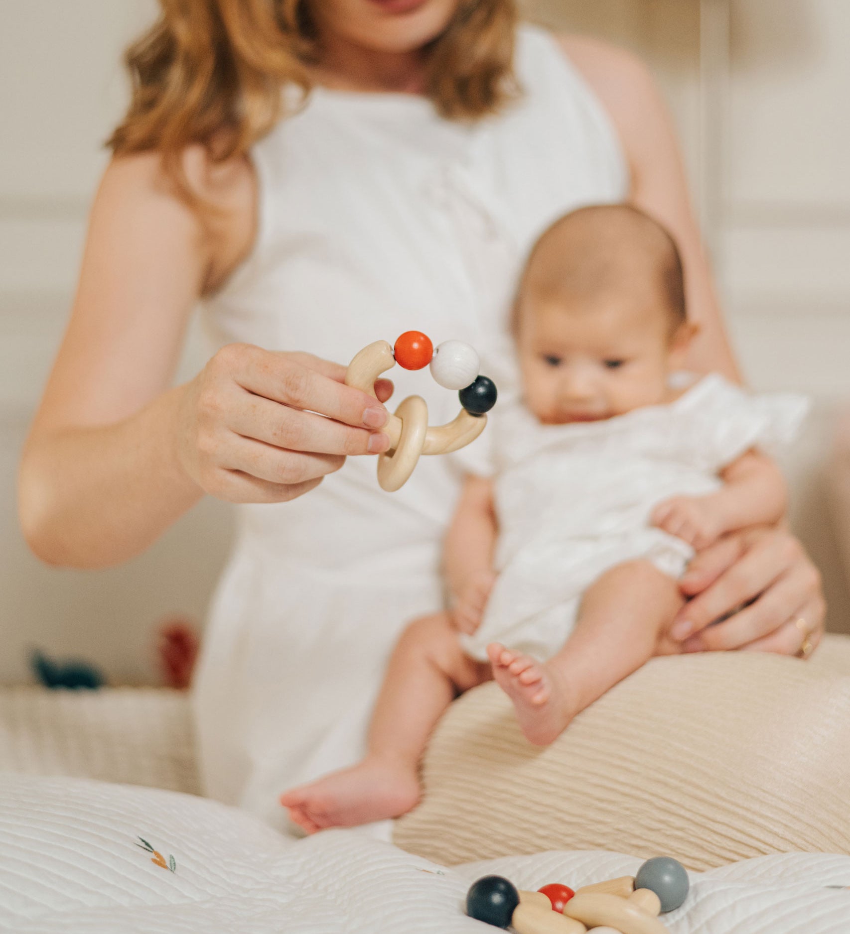 An adult holding a baby on their lap with a PlanToys Beads Rattle in a High Contrast colourway in their other hand. PlanToys range of toys are made from sustainably sourced rubberwood, we're proud stockists of PlanToys here at Babipur. 