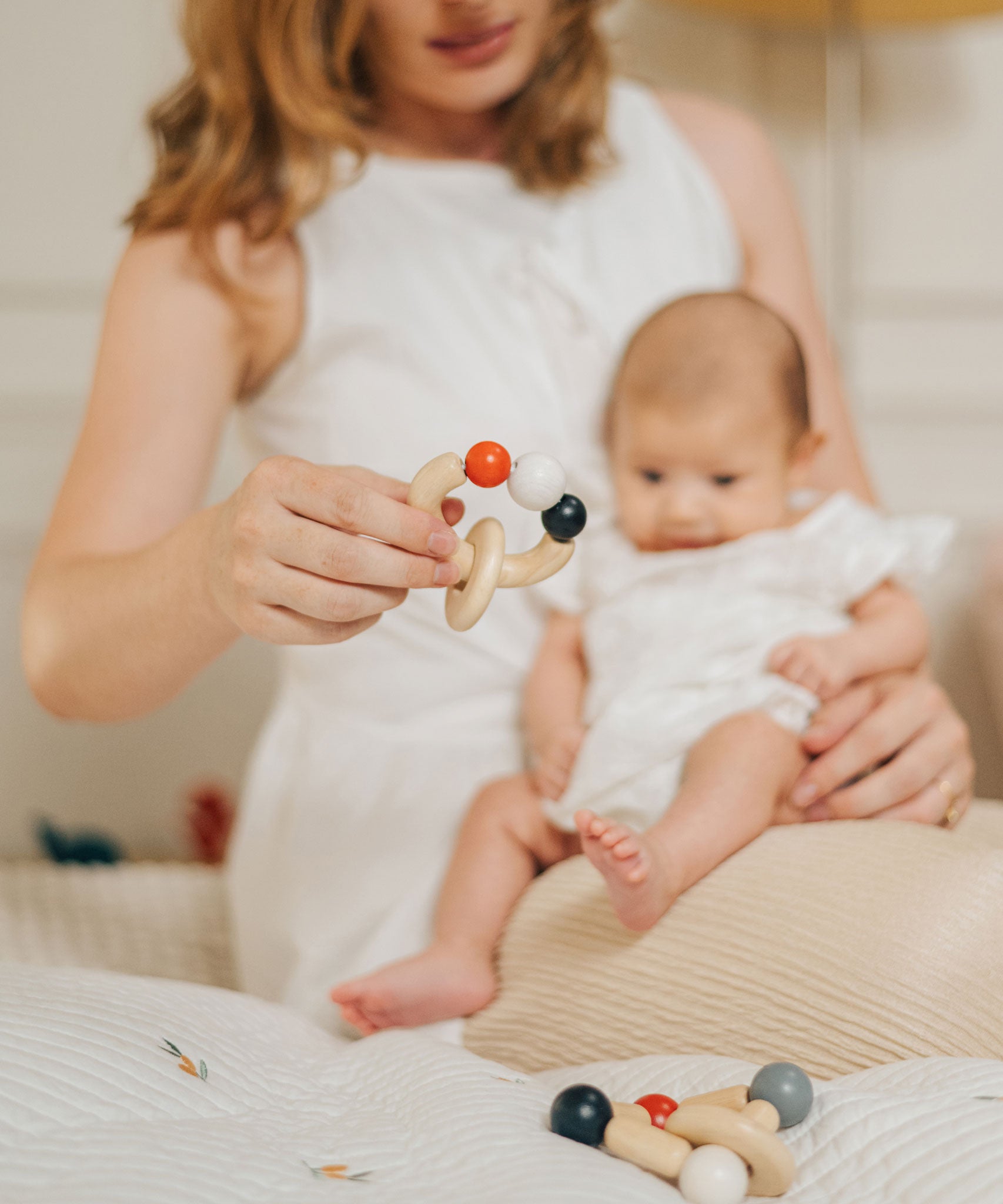 An adult holding a baby on their lap with a PlanToys Beads Rattle in a High Contrast colourway in their other hand. PlanToys range of toys are made from sustainably sourced rubberwood, we're proud stockists of PlanToys here at Babipur. 