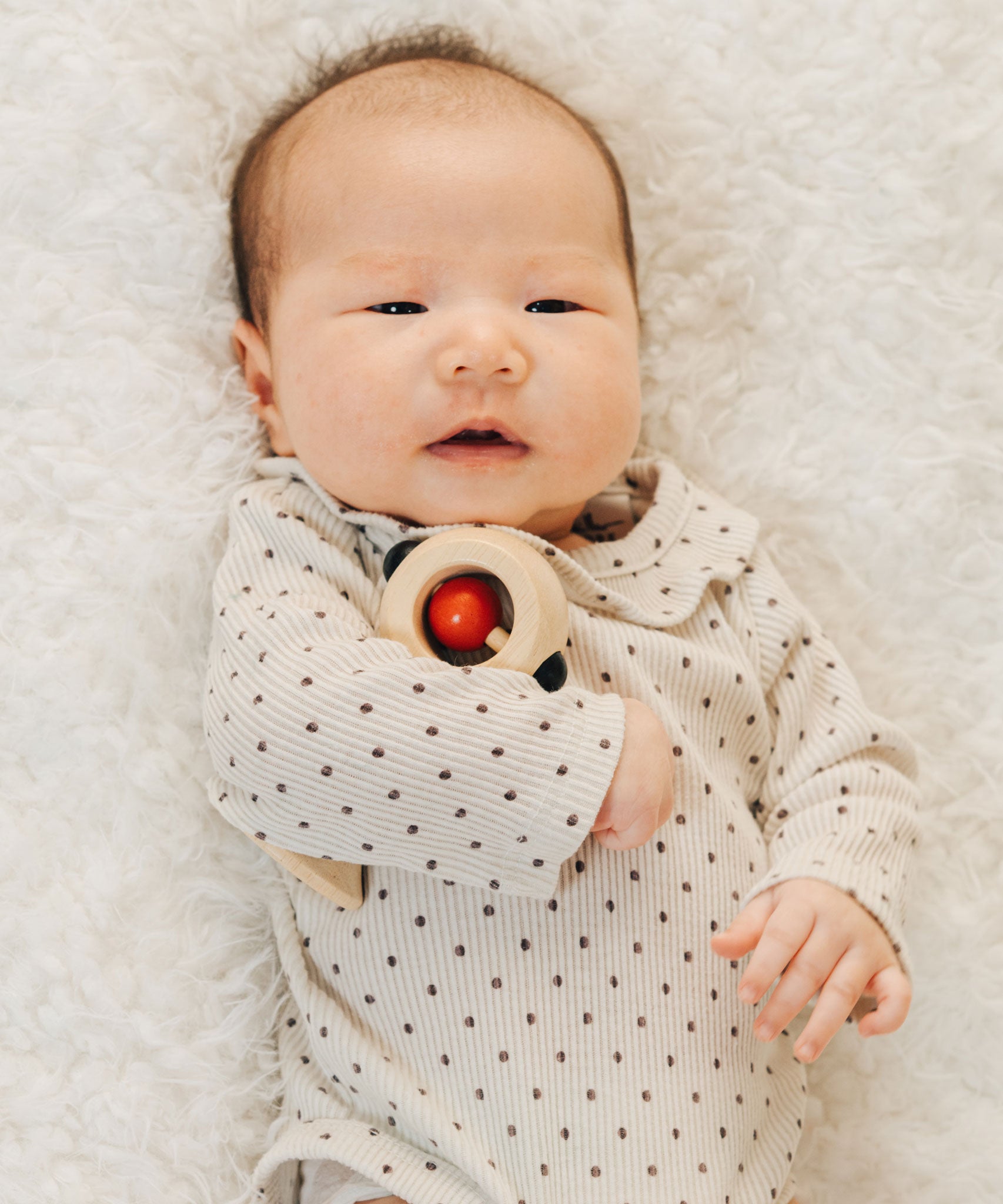 A baby with a PlanToys Shaking Rattle in a High Contrast colourway under their arm. The red and black details stand out against the natural rubberwood body. PlanToys range of toys are made from sustainably sourced rubberwood, we're proud stockists of PlanToys here at Babipur. 