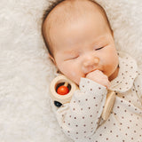 A baby holding the PlanToys Shaking Rattle in a High Contrast colourway under their arm. The red and black details stand out against the natural rubberwood body. PlanToys range of toys are made from sustainably sourced rubberwood, we're proud stockists of PlanToys here at Babipur. 