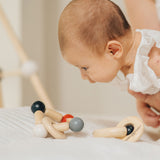 A baby being held up, the baby is looking at a PlanToys Beads Rattle in a High Contrast colourway that has been placed on the surface below them. 
PlanToys range of toys are made from sustainably sourced rubberwood, we're proud stockists of PlanToys here at Babipur. 