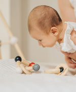 A baby being held up, the baby is looking at a PlanToys Beads Rattle in a High Contrast colourway that has been placed on the surface below them. 
PlanToys range of toys are made from sustainably sourced rubberwood, we're proud stockists of PlanToys here at Babipur. 