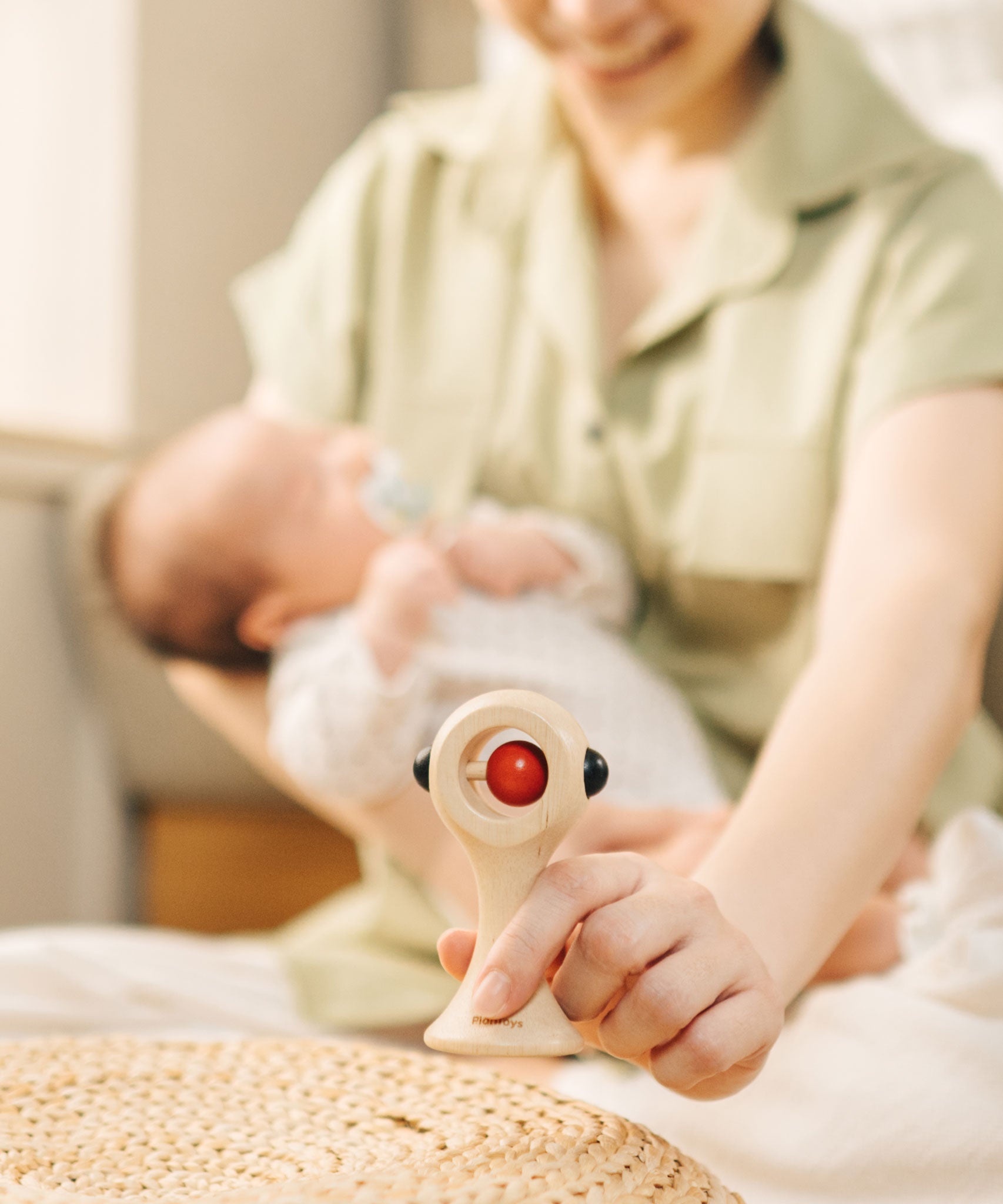 An adult placing a PlanToys Shaking Rattle in a High Contrast colourway on a table in front of them. The red and black details stand out against the natural rubberwood body. PlanToys range of toys are made from sustainably sourced rubberwood, we're proud stockists of PlanToys here at Babipur. 