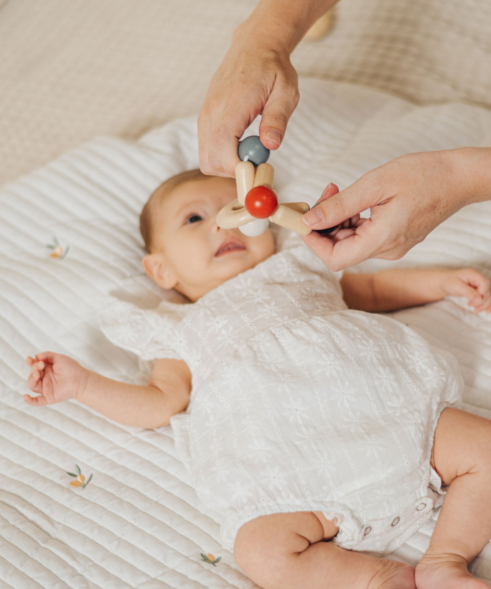 An adult holding the PlanToys high contrast square clutching toy above a baby. PlanToys range of toys are made from sustainably sourced rubberwood, we're proud stockists of PlanToys here at Babipur. 