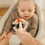 An adult's hand holding up the PlanToys high contrast Triangle baby Clutching Toy in front of a baby. A black and natural wood wooden ball in a stretchy triangle clutching toy. PlanToys range of toys are made from sustainably sourced rubberwood, we're proud stockists of PlanToys here at Babipur. 
