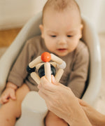 An adult's hand holding up the PlanToys high contrast Triangle baby Clutching Toy in front of a baby. A black and natural wood wooden ball in a stretchy triangle clutching toy. PlanToys range of toys are made from sustainably sourced rubberwood, we're proud stockists of PlanToys here at Babipur. 