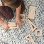 An overhead view of a child sitting on a patterned rug playing with the PlanToys Hollow Blocks.