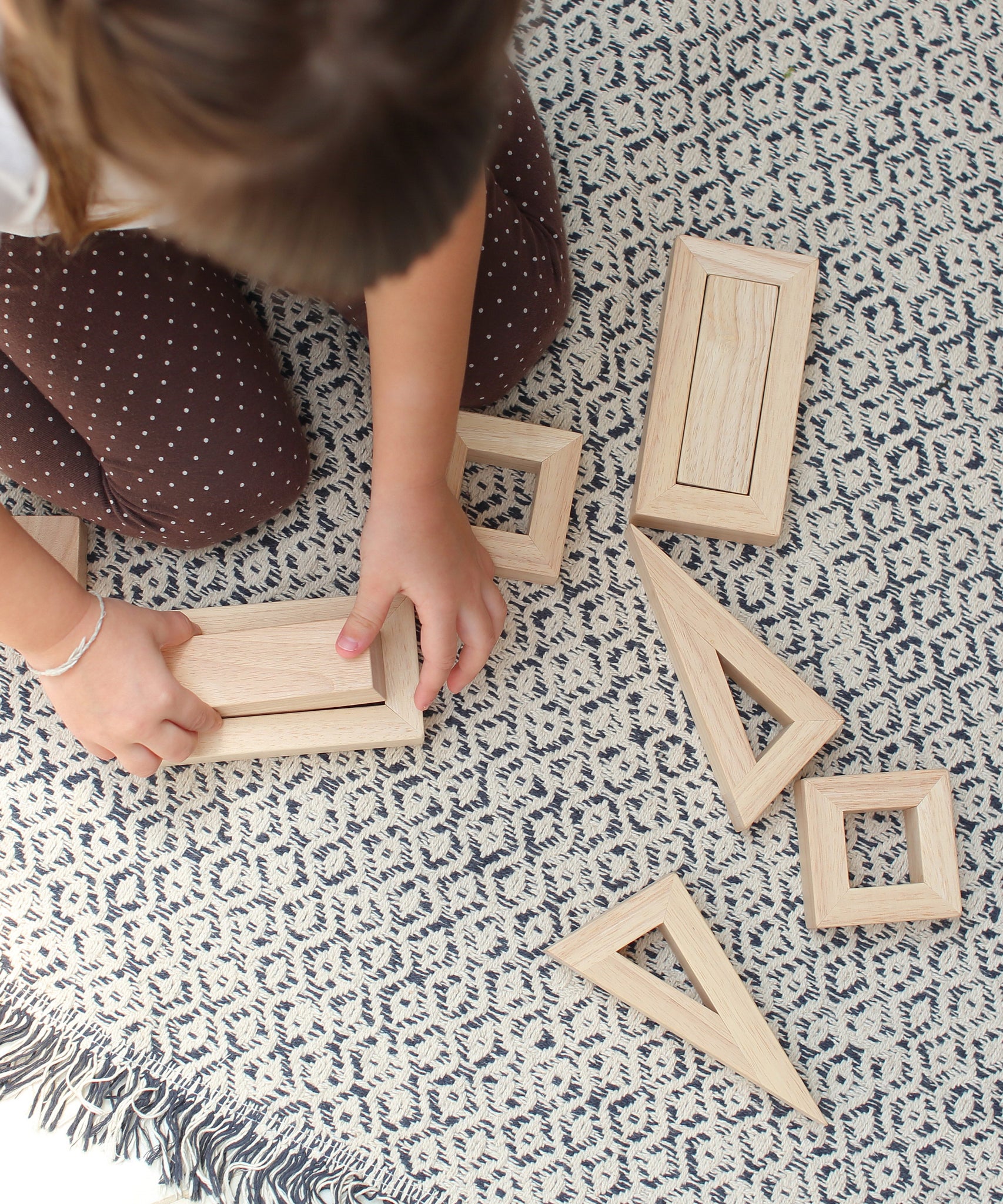 An overhead view of a child sitting on a patterned rug playing with the PlanToys Hollow Blocks.