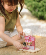Child playing with the PlanToys ice cream shop wooden toy playset placing the ice creams on a stand at the front of the shop.